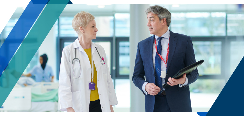 Two healthcare executives conversing in a facility hallway Two healthcare executives conversing in a facility hallway